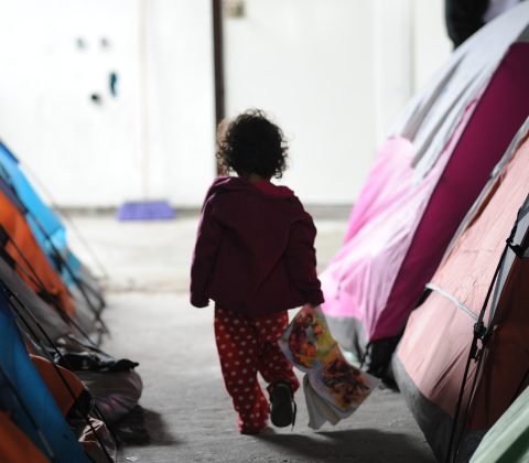 Girl amongst tents holding bear seeking asylum